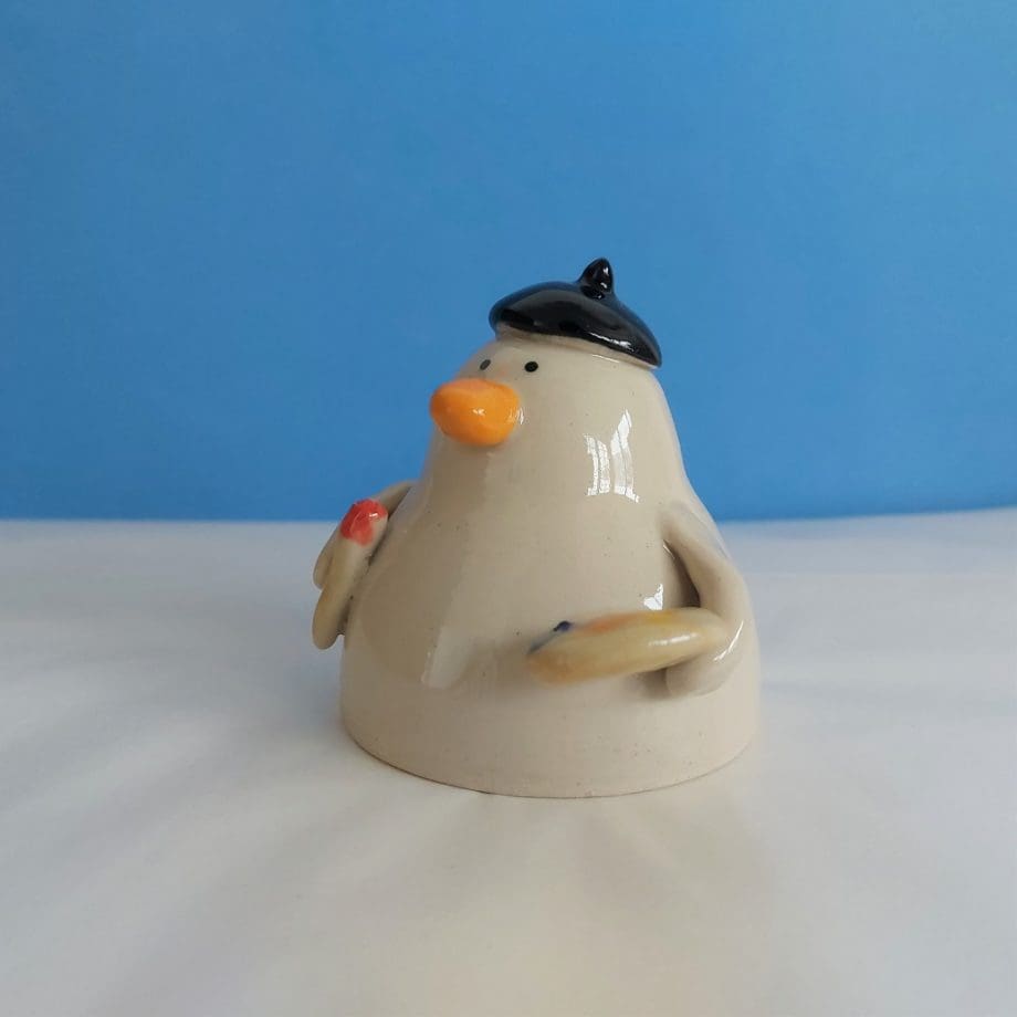 A handmade ceramic duck ornament with a beret, paint brush and paint pallette